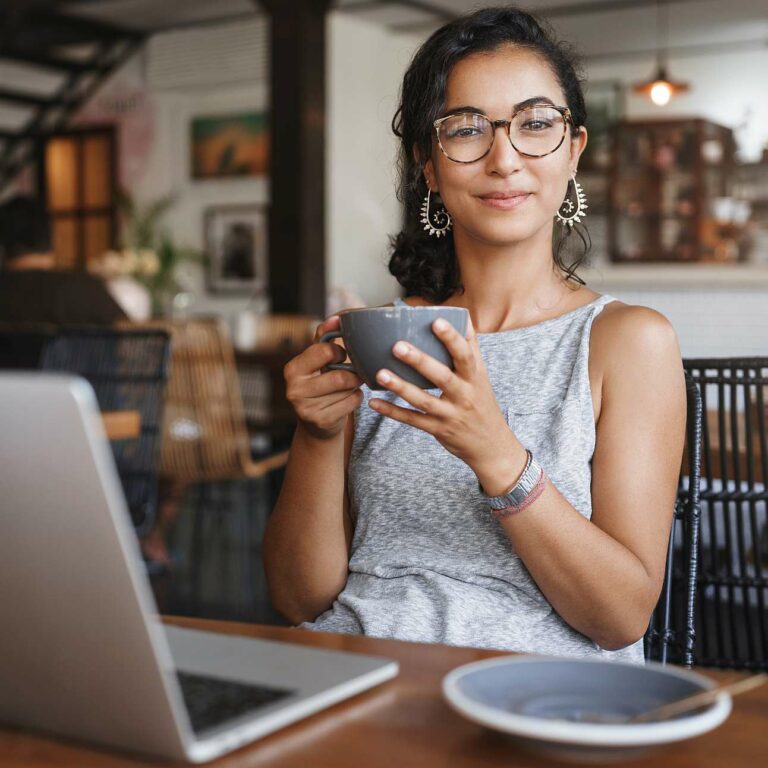 Relaxation, urban people and education concept. Charming young female freelancer, student having break from work, order coffee, holding cup and enjoy cappuccino, smiling pleased, using laptop.